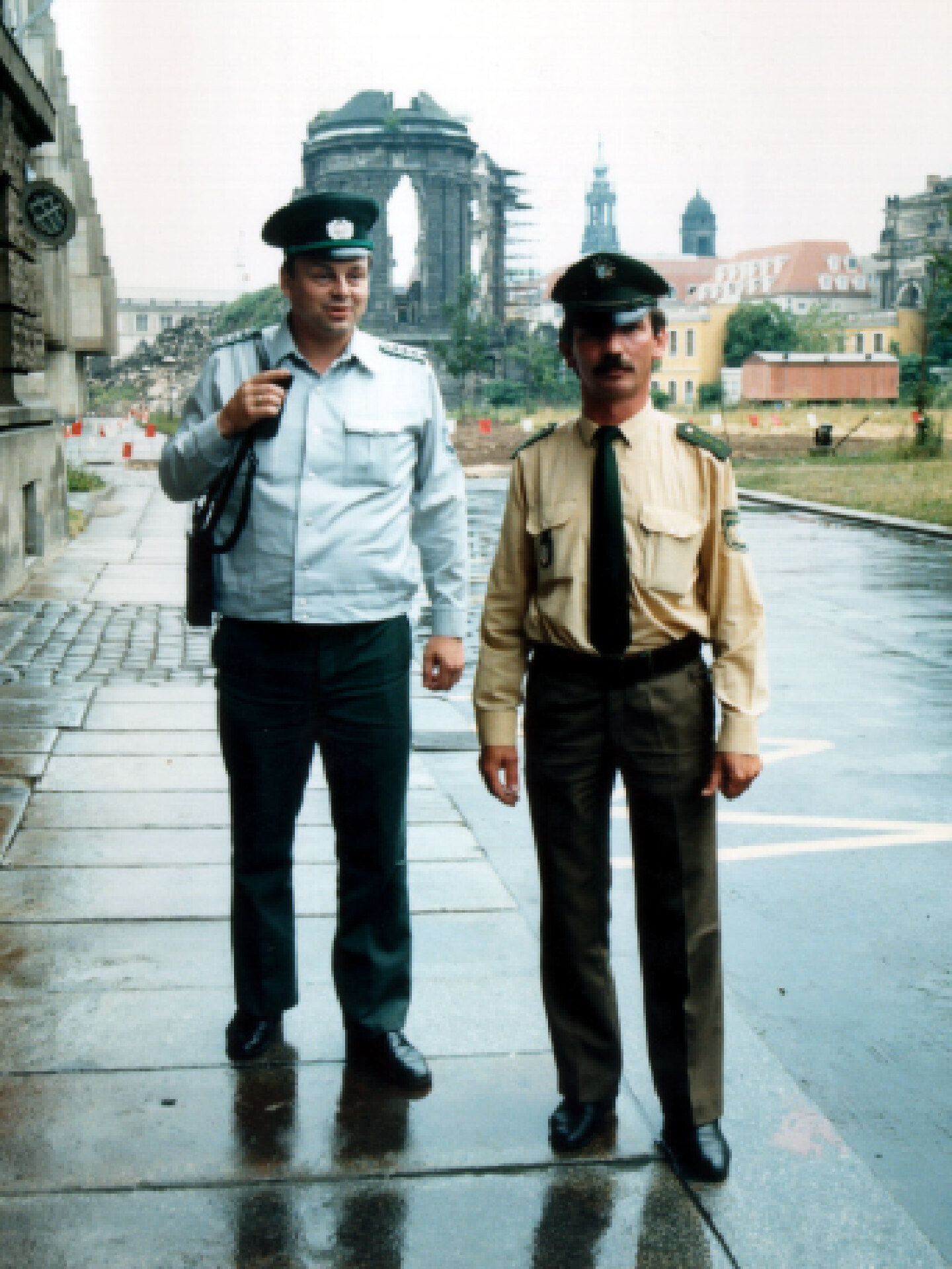 Das Farbfoto zeigt zwei Polizisten auf einem Fußweg in Dresden. Der linke Polizist trägt eine blaue Uniform, der rechte Polizist stammt aus Bayern und trägt eine grün-beige Uniform.
