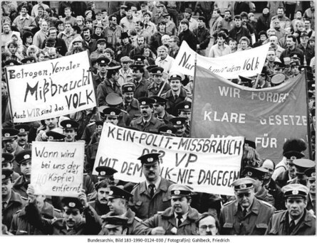 Eine dicht gedrängte Menge bei einer Demonstration, die Mehrzahl der Demonstranten trägt Uniform. Die Menschen auf dem Bild halten fünf Transparente in die Höhe, eine der Aufschriften ist: »Betrogen, Verraten Mißbraucht Auch WIR sind das VOLK«.