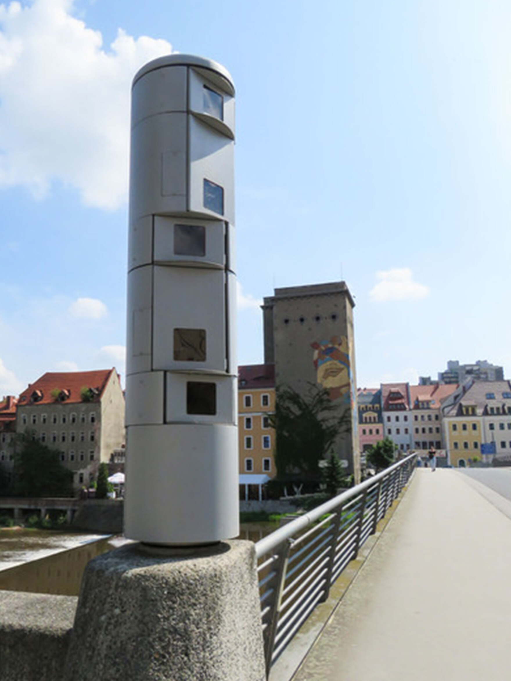 Im Vordergrund steht die graue Kamerasäule mit fünf Linsen auf der Altstadtbrücke in Görlitz. Im Hintergrund erkennt man einige Häuser der Stadt.