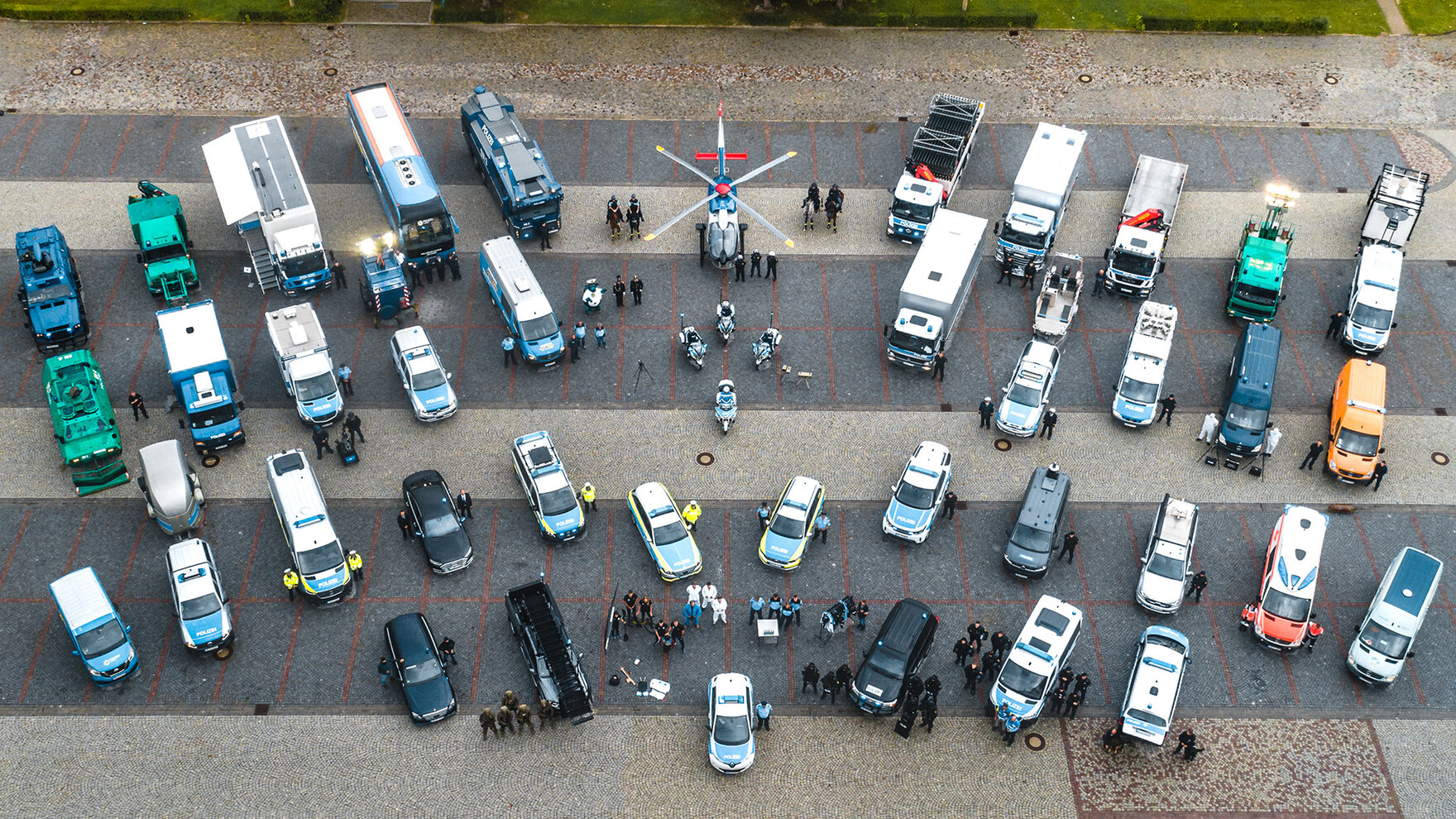 Aus der Vogelperspektive fotografiert sind die unterschiedlichen Bereiche der Polizei Sachsen. Es ist ein Hubschrauber zu sehen, viele unterschiedliche Fahrzeuge wie Streifenwagen bis zu Wasserwerfer, Motorräder und Busse. Daneben die Bediensteten.