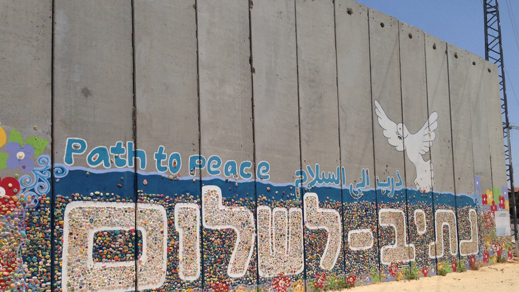 Der Foto-Schnappschuss zeigt die Sperranlage zum Gazastreifen. Auf der grauen Mauer sind bunte Zeichnungen. Unter anderem sieht man eine Friedenstaube und den Schriftzug »Path to peace«.