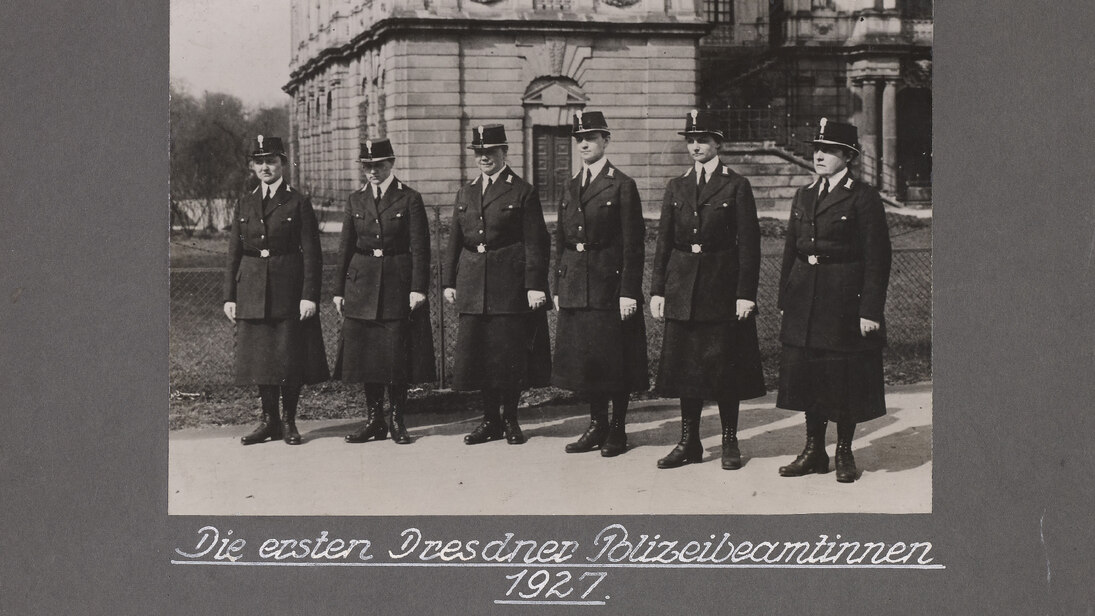 Eine historische Schwarz-Weiß-Fotografie zeigt sechs Polizeibeamtinnen in ihrer Uniform, die für das Foto in einer Reihe stehen. Teil der Dienstkleidung sind je ein langer Rock und eine Kopfbedeckung.